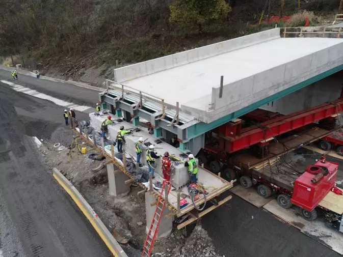 An aerial image taken from a drone showing construction workers placing a bridge segment over a roadway.